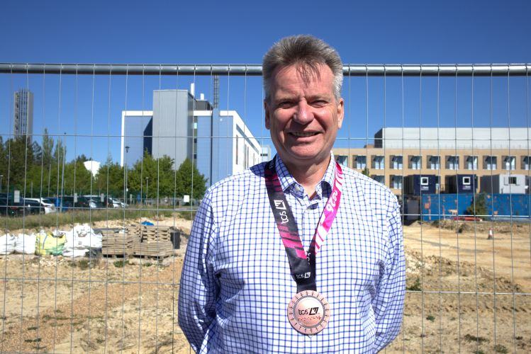 A man wearing a London marathon medal smiling outside a construction hospital site
