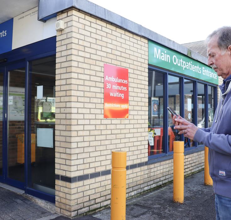Volunteer Mike using CUH Directions app on a mobile phone, standing outside the outpatients' department