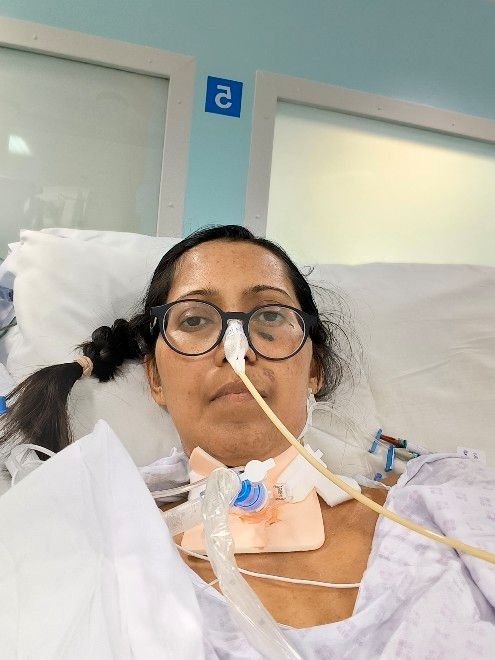 A woman with hospital tubes on her nose, in a hospital gown in intensive care