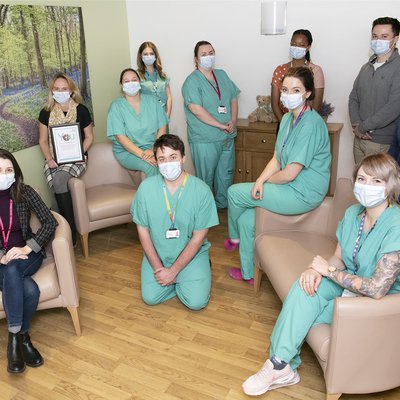 12 members of the mortuary team, either standing or sitting, all socially distanced and wearing surgical masks. One is holding the team's You Made a Difference certificate.