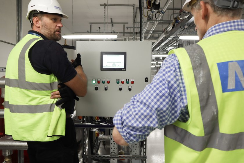 Two men wearing yellow high-viz looking at computer panel