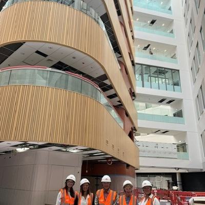 Project team are pictured standing in the Atrium at Moorfields Eye Hospital in London, it is still under construction, they are wearing high-vis and hard hats and smiling at the Camera.