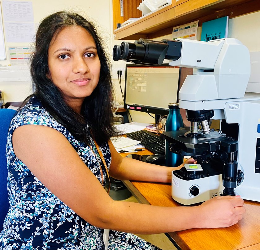 Picture of Saranja Rishikeson sitting at a desk with a microscope