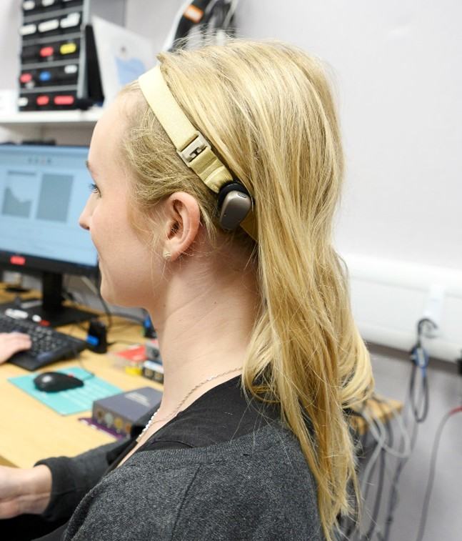 Person wearing a headband-style hearing device while seated at a workstation with audio equipment