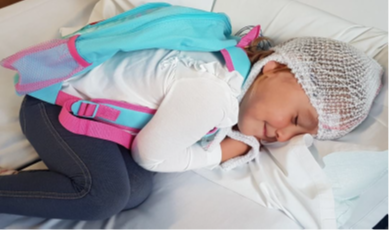 The image shows a person lying on a white bed or padded surface indoors. The surface appears soft and layered, resembling bedding or a mattress with white sheets or covers.