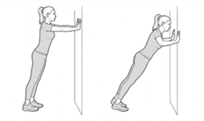 Wall push-up exercise, leaning toward a wall with hands placed on it and then pushing back to the starting position.