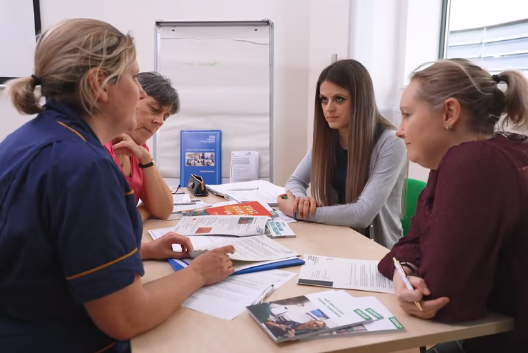Staff and patients sat round a table talking and looking at leaflets