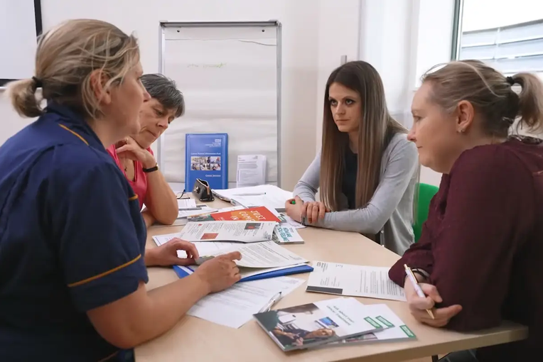 Staff and patients sat round a table talking and looking at leaflets