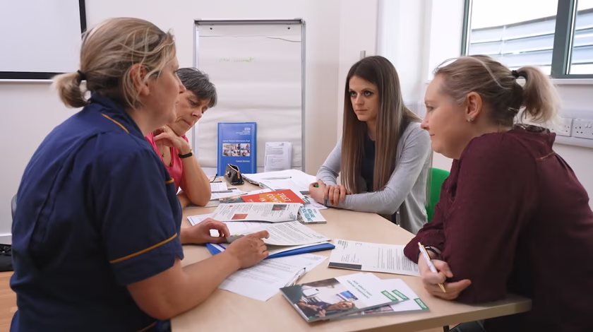 Staff and patients sat round a table talking and looking at leaflets