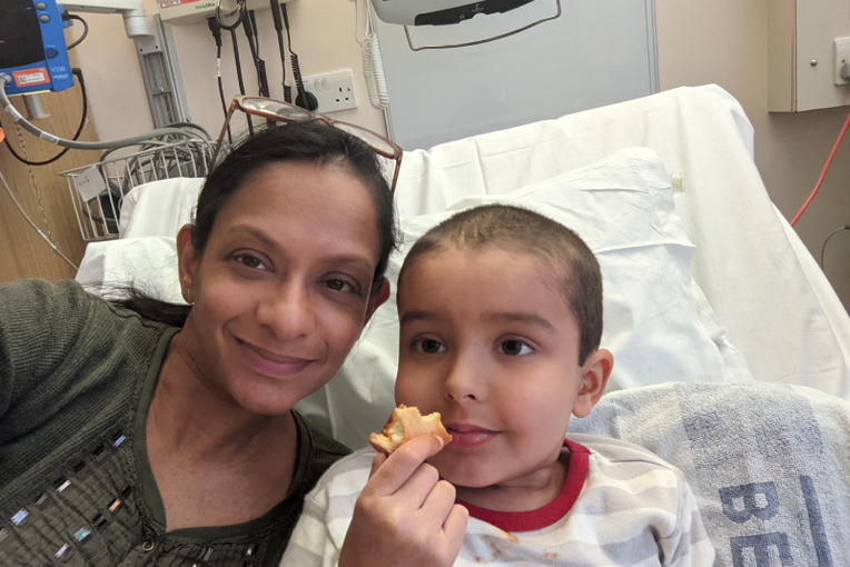 A selfie of Razia sitting on a hospital bed next to Zayan who is eating.