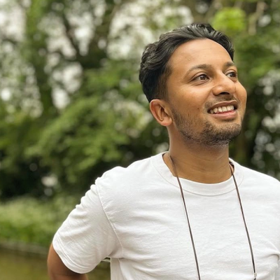 Sameer wearing a white t-shirt standing on a canal boat with trees in the background