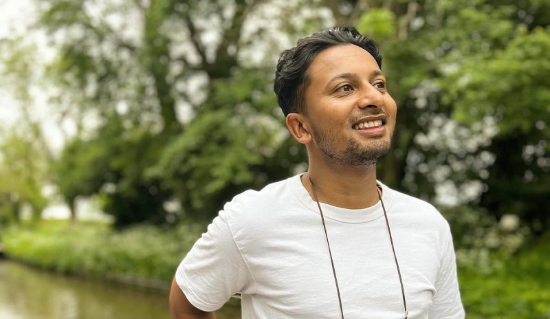 Sameer wearing a white t-shirt standing on a canal boat with trees in the background
