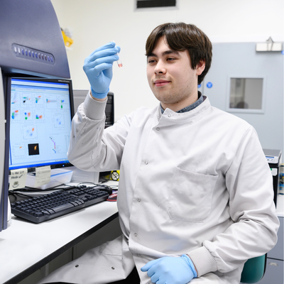 Sammy Ellis wearing white coat in lab, holding up a vial containing a fluid