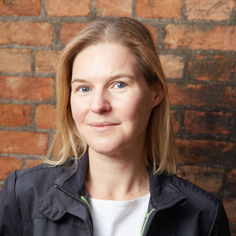 A photo of a lady wearing a suit with a brick wall in the background
