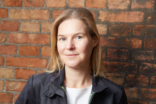 A photo of a lady wearing a suit with a brick wall in the background