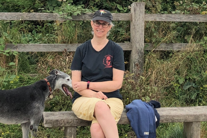 Sarah, sitting on a bench in the countryside facing the camera, with her dog, Mike, standing next to her.
