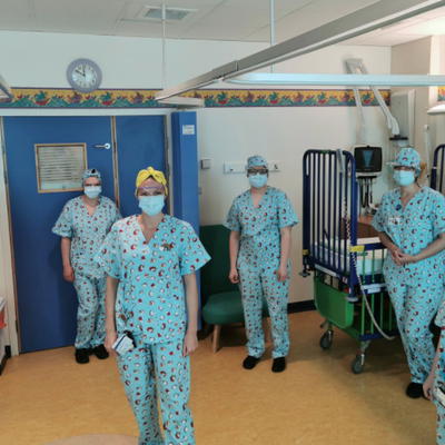 Six members of staff are all wearing matching handmade penguin scrubs standing up and looking at the camera in a hospital ward.