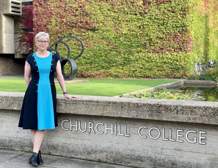 Professor Sharon Peacock standing outside Churchill College wearing a black and blue dress