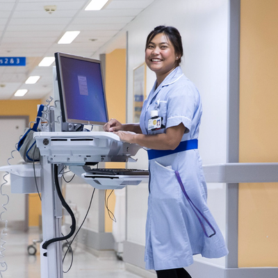 A nurse using a workstation on wheels in a hospital corridor