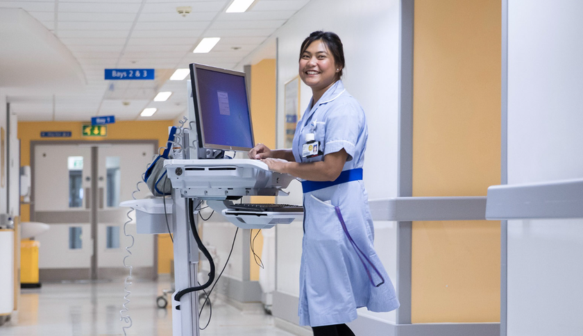 A nurse using a workstation on wheels in a hospital corridor