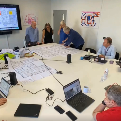 Cambridge Children's Hospital team are gathered around a desk looking at colourful floor plans on a big screen, there are paper floorplans on the desk.