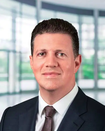 A headshot of a man with short dark hair, dark eyes and a smart suit and tie
