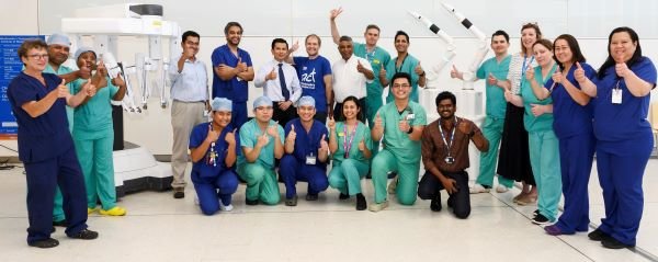 THUMBS UP: Mr Siong-Seng Liau (sixth on right back row) and the wider team celebrate the first anniversary of the new robots (left: Da Vinci Xi, right: CMR Versius).