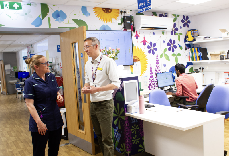 Members of staff talking and working around the reception desk in T2 with floral prints and display screens on the wall behind them.
