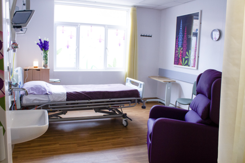 A room in ward T2 including a bed and armchair. On the wall and windows are large decorative stylised prints of flowers.