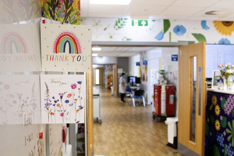 Several thank you cards stuck to the wall opposite the reception desk of T2, in the background is more of the ward and the colourful wall prints.