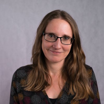 a woman with long brown hair and glasses, smiling