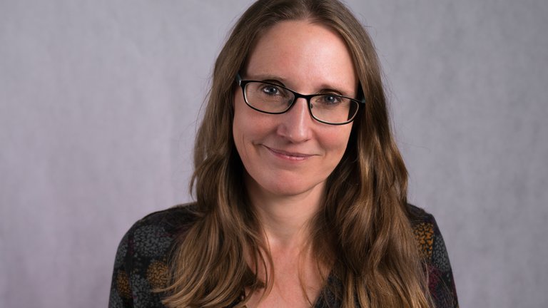 a woman with long brown hair and glasses, smiling