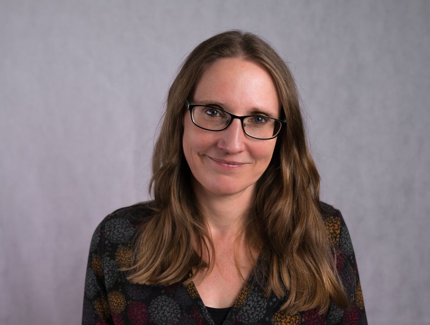 a woman with long brown hair and glasses, smiling