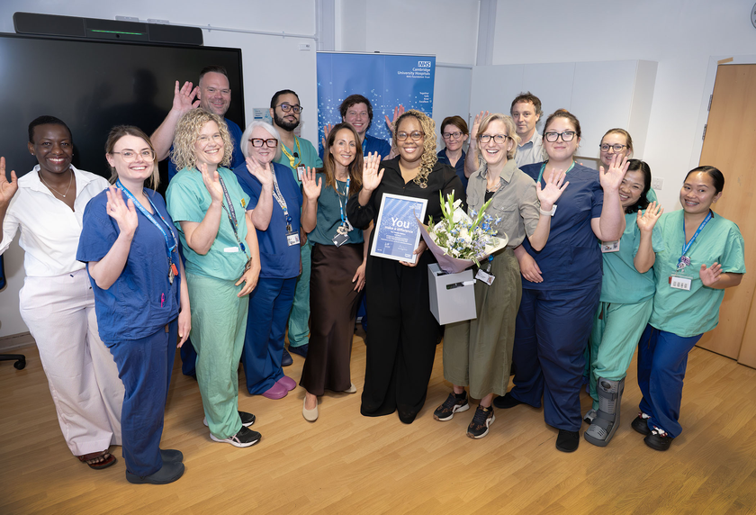 Tara Walters with her colleagues waving to camera, all smiles, there's also a cake there, flowers and the prospect of celebrations