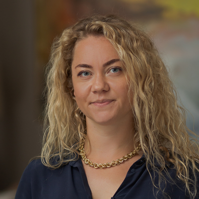A woman with long curly blond hair, with a black shirt and shiny beads