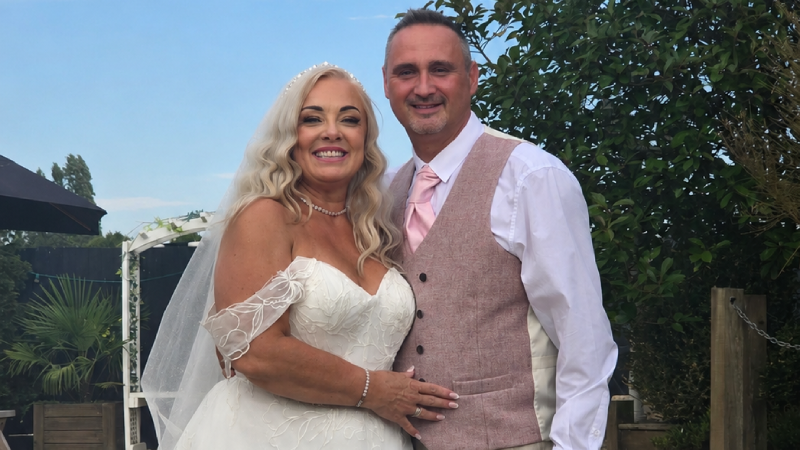 Victoria in a wedding dress standing with Mark in a suit outside in a garden