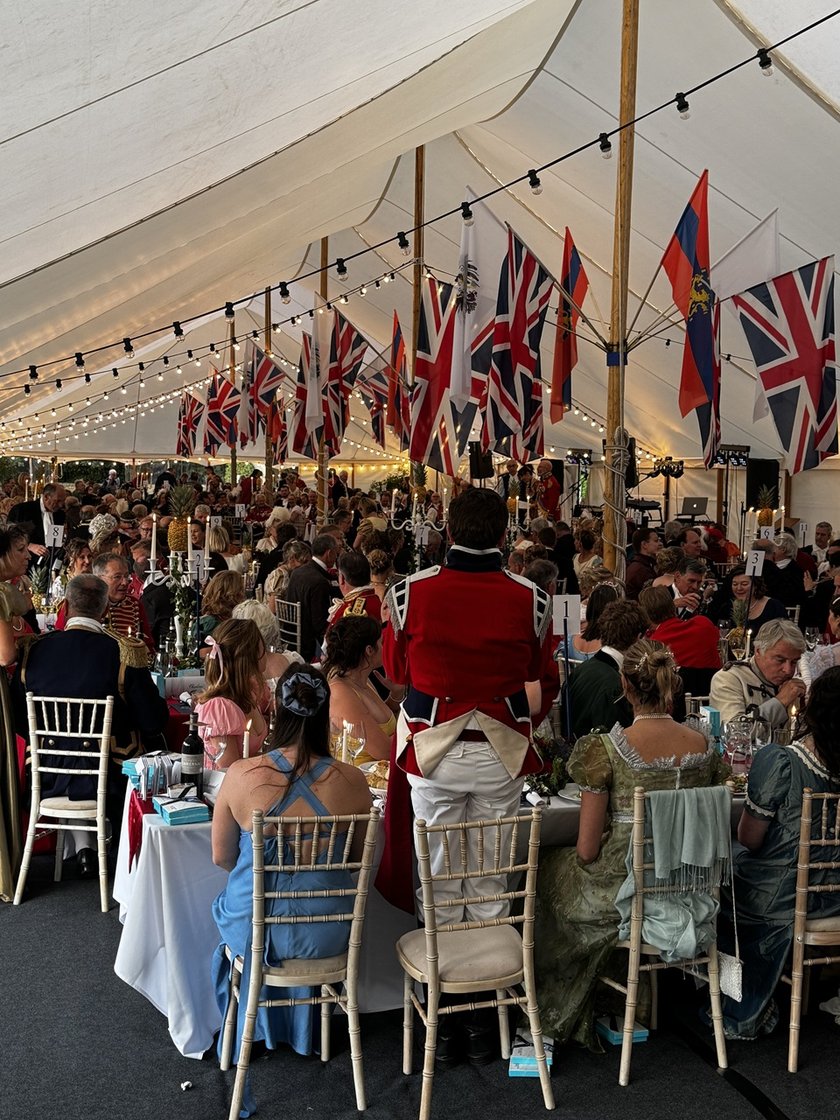 The inside of a marquee decoration with union jack flags, with lots of people sitting at dinner tables in formal dress