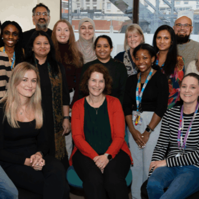 A group of 17 people sat and standing together in an office space smiling at the camera