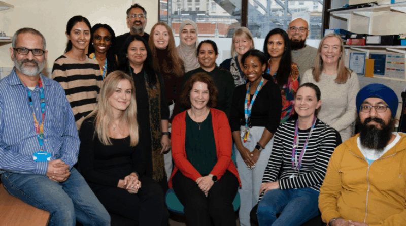 A group of 17 people sat and standing together in an office space smiling at the camera