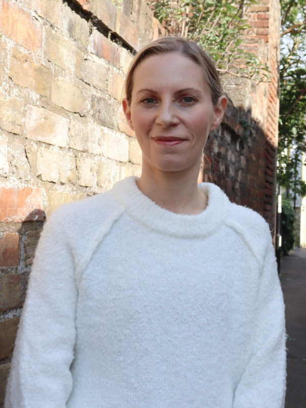 Woman standing by wall outside on a sunny day