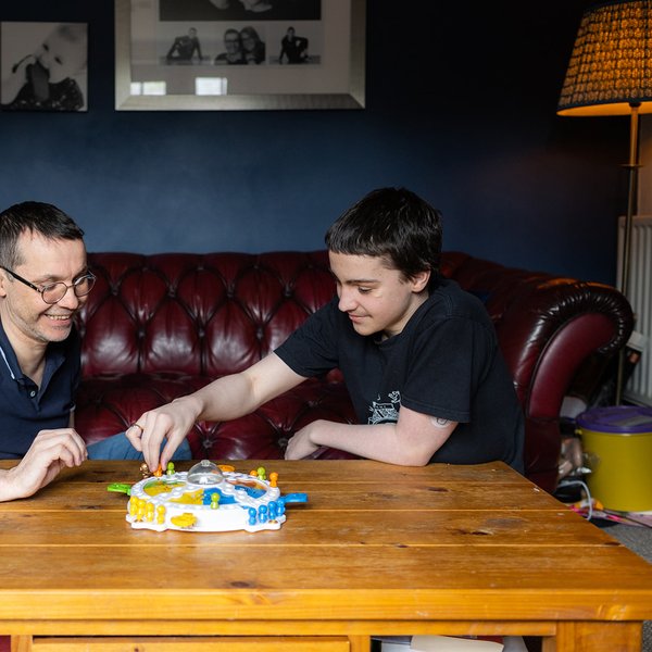 A teenage boy and his dad playing the board game frustration in their living room. the room has dark blue walls and a dark red leather sofa