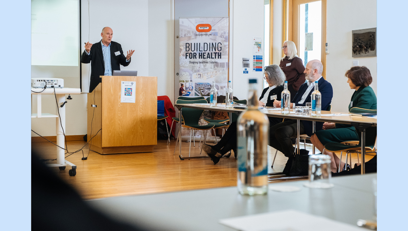 A man in a suit presenting to a room full of people. There is a banner behind him saying Bouygues UK, Building for Life
