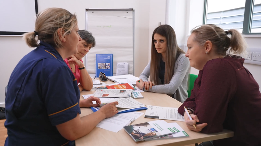 four members of the cancer participation group sat at a table looking at and discussing the contents of a cancer patient information pack.