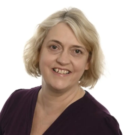 Debi looking into the camera on a white background wearing a dark v neck top
