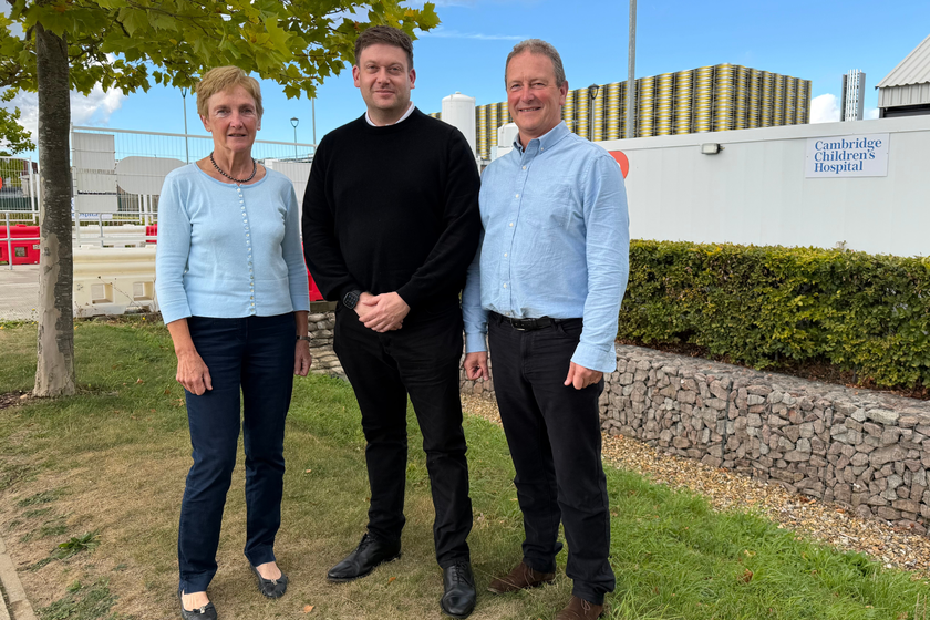 A woman and two men standing by the Cambridge Children's hospital collaboration hub, which is a white portacabin on the construction site