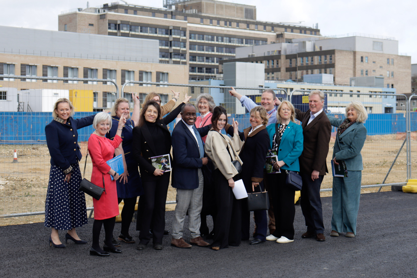 A group of people standing outside the Cambridge Children's Hospital site on a sunny day pointing.