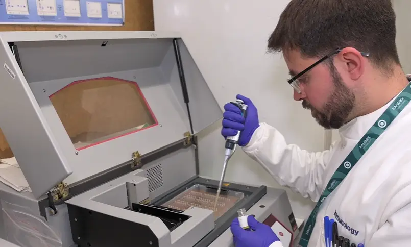 A member of the immunology team in the immunology lab. The person is wearing blue gloves and has a small bottle in one hand and a large pipette in the other.
