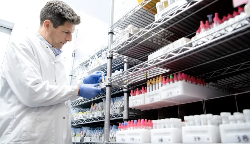 Member of staff in a white lab coat looking at test tubes and vials on shelves