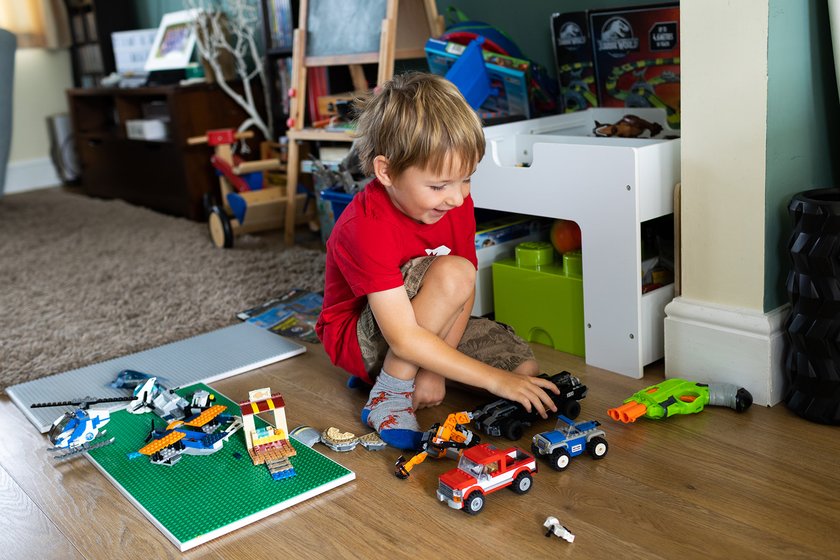 A young boy with blond hair and a red t shirt playing with lego in his living room