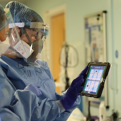 Two members of staff are dressed in full PPE looking at a graphics tablet